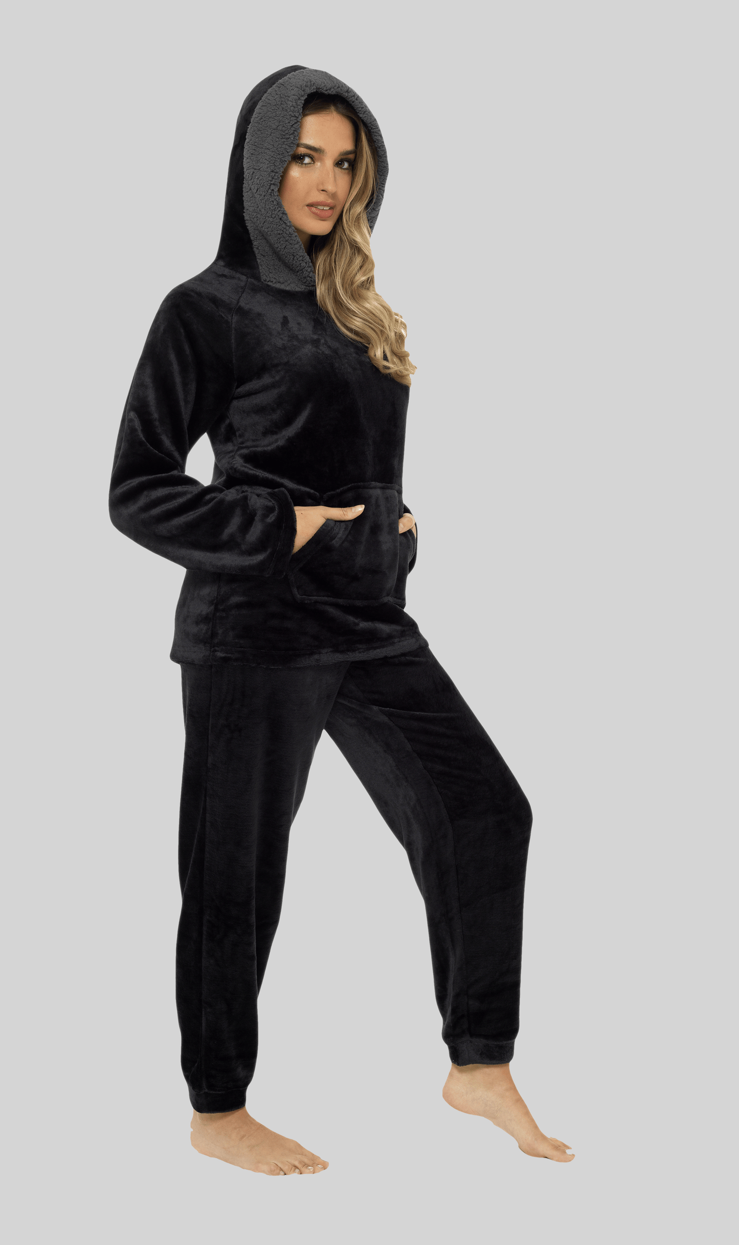 Woman wearing a black velour tracksuit on a gray background